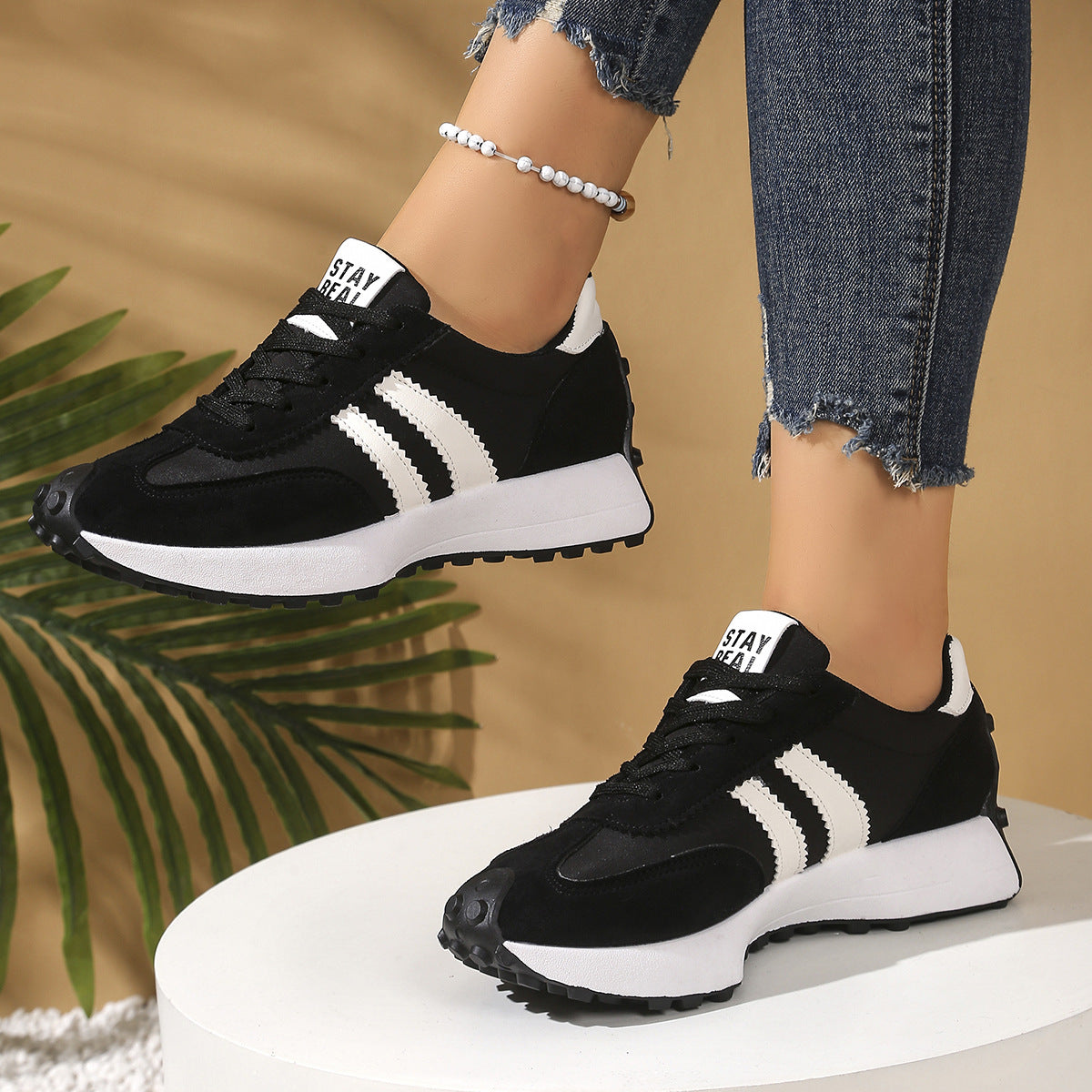 Black and white lace-up sneakers with striped side panels, thick soles, and "STAY REAL" tongue branding.