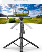 Black 360-degree auto-tracking phone tripod with foldable legs and a mounted smartphone filming a panoramic landscape.