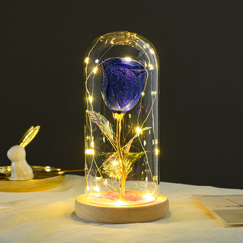 A sparkling blue glitter rose in a glass dome with LED fairy lights on a wooden base.