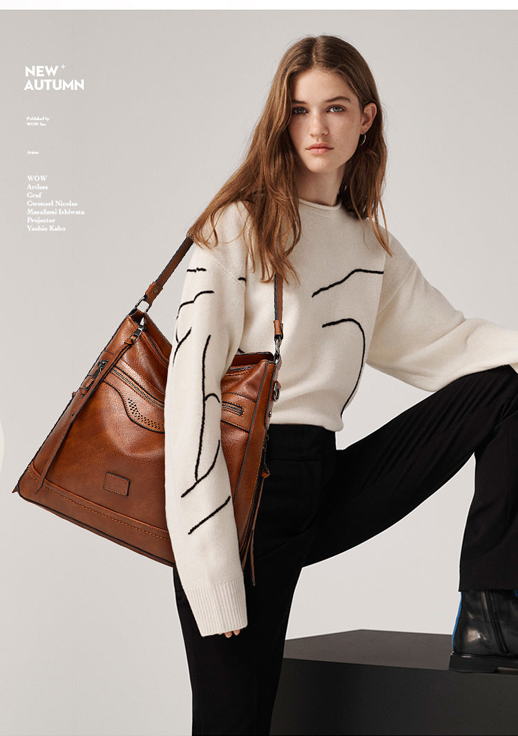 Model carrying a vintage-style brown soft leather one-shoulder tote bag with zipper and stitching details.