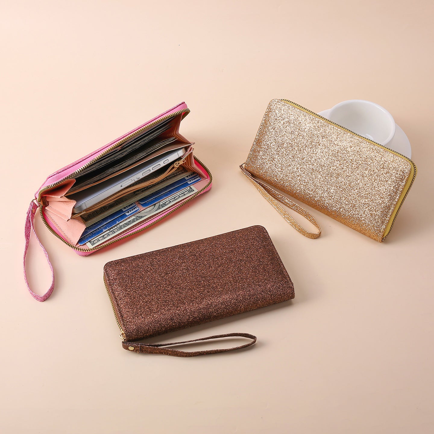 Three glittery, multi-functional zippered wristlet clutches in pink, gold, and brown, featuring card slots and storage.