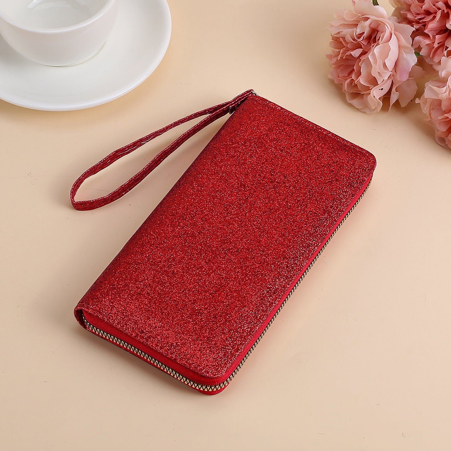 A shiny red glitter clutch for women with a wrist strap and gold zipper closure, set against a light background.