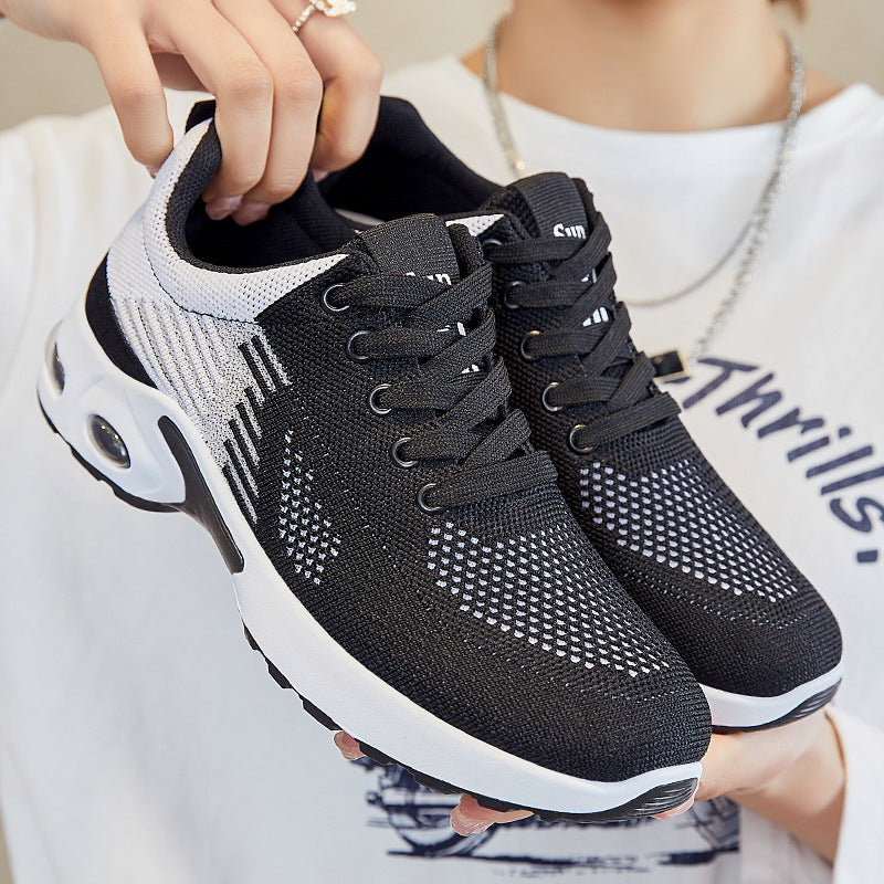 Black and white knit lace-up running shoes with air-cushioned white soles, held in hand.