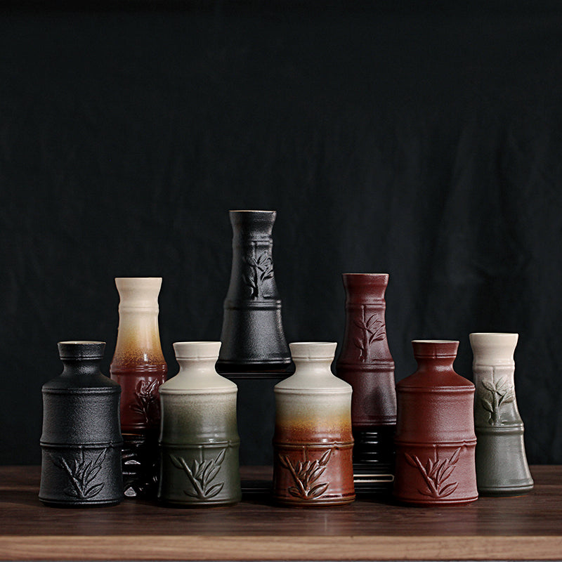 A set of ceramic sake pots in black, red, and green gradients with raised bamboo patterns on a wooden surface.