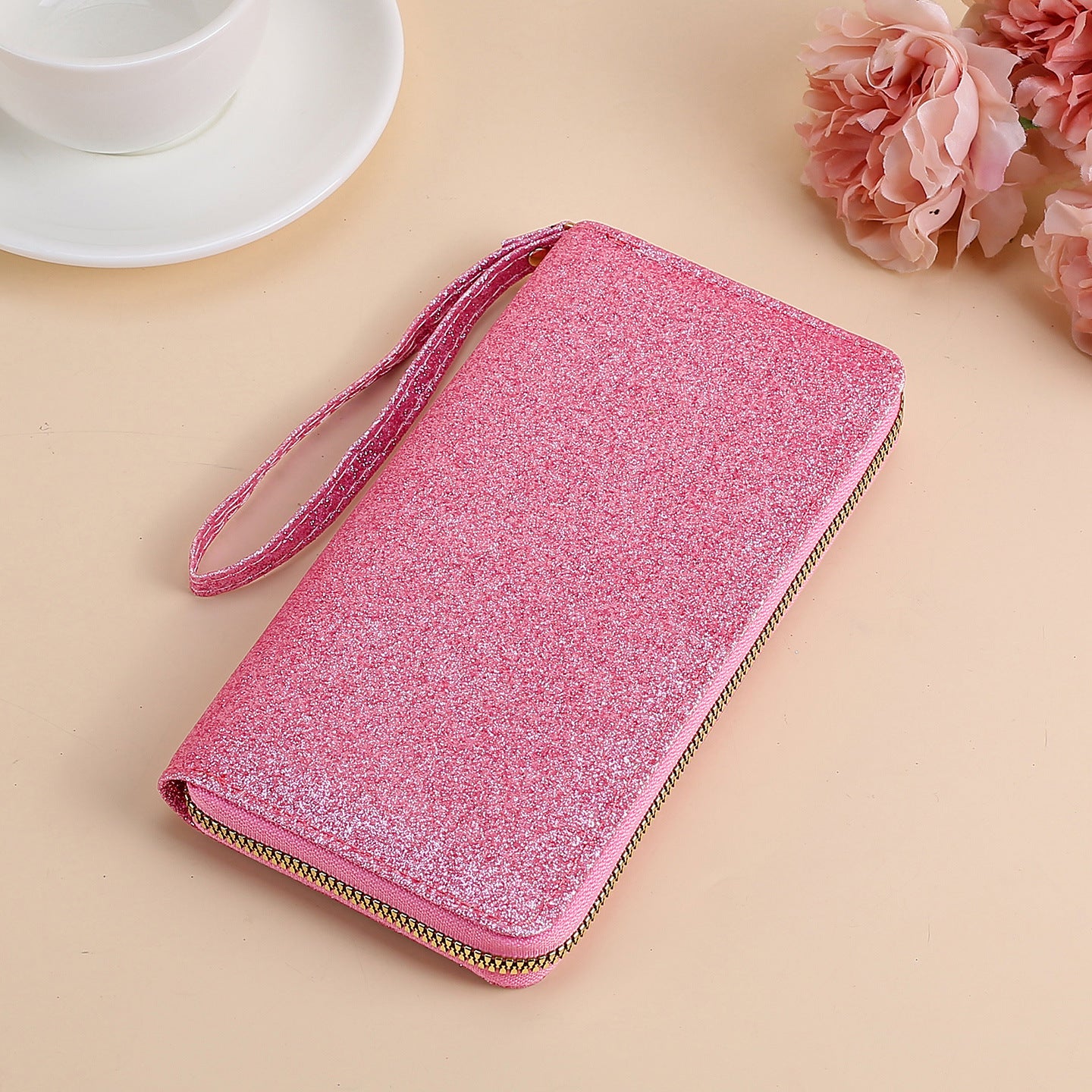 A sparkling pink glitter clutch with a wrist strap and gold zipper closure.