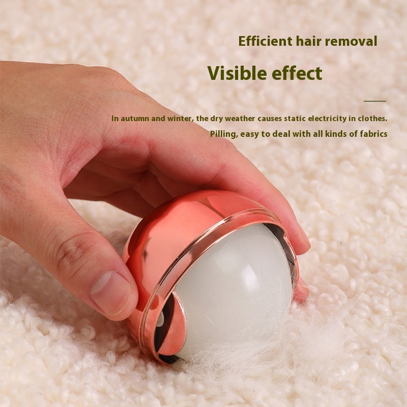Hand holding a rose-gold, spherical, washable gel lint roller, used to remove pet hair from textured white fabric.
