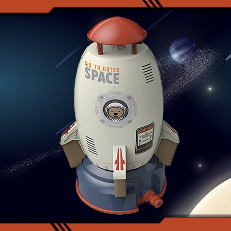 White and blue plastic rocket sprinkler toy with red top, space graphics, and bear astronaut window decal.