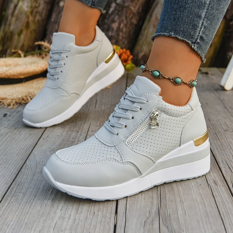 Light gray perforated wedge sneakers with white soles, side zippers, and gold heel accents on a wooden background.
