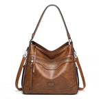Brown vintage-style soft leather tote bag with a top handle, shoulder strap, zippered pockets, and perforated details.