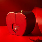 Red apple-shaped jewelry box with a gold heart knob and leaf accent, set against a matching red background.