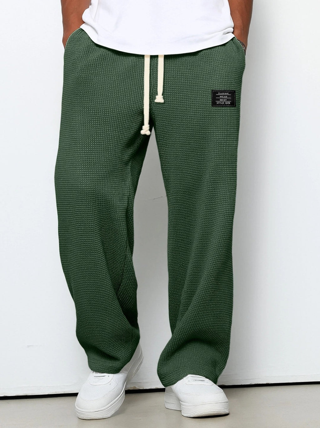 Dark green waffle-knit straight pants with a white drawstring, loose fit, and a small black rectangular brand patch.