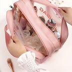 Hands opening a pink, clear travel makeup bag filled with toiletries and bottles, showing organized compartments.