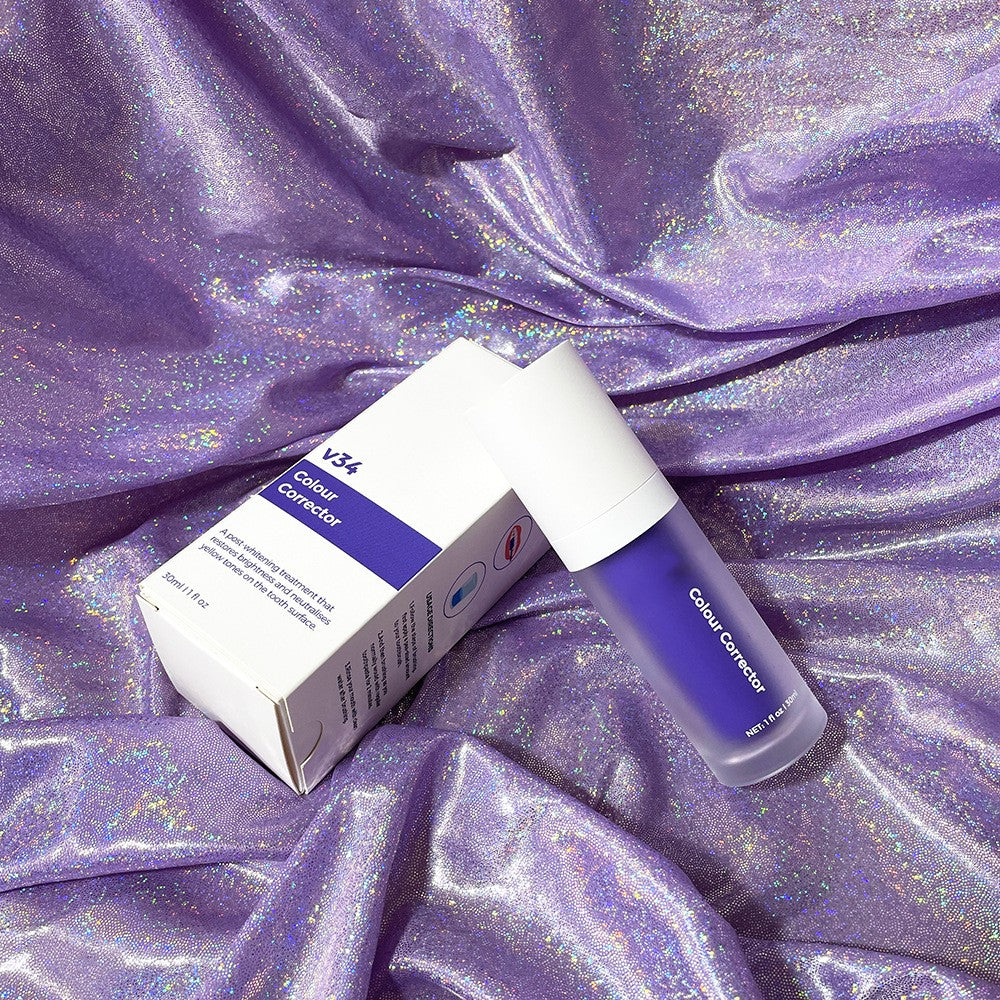 V34 purple teeth whitening mousse pump and box on a shimmering, light-reflecting purple fabric background.