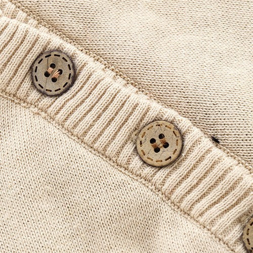 Close-up of beige knitted baby clothes featuring ribbed trim and round wooden-style buttons.