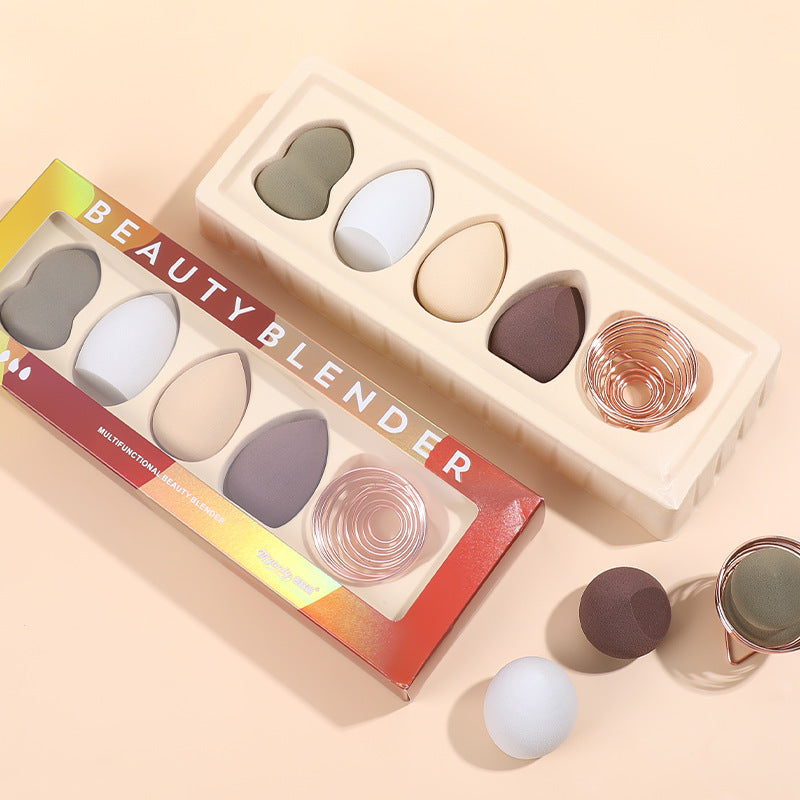 A set of colorful, teardrop-shaped makeup sponges in packaging with a rose gold metal drying stand.