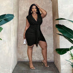 Woman in a black V-neck, ruched waist-tie dress with a ruffled hip detail, standing in a stone archway.