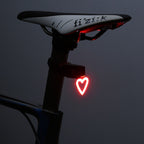 Heart-shaped red LED bike taillight mounted on a bicycle seat post against a dark background.
