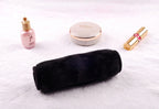 A plush black makeup remover towel on a white surface, accompanied by a small pink bottle, compact, and lipstick.
