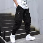 Black cargo joggers with drawstring waist, side flap pockets, and ribbed cuffs. Styled with a white tee and sneakers.