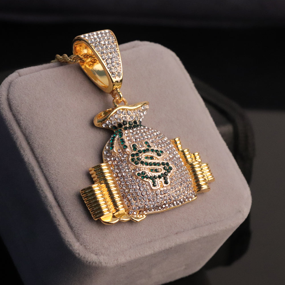 Gold hip-hop money bag pendant covered in clear crystals with green rhinestone dollar sign detail on a gray cushion.