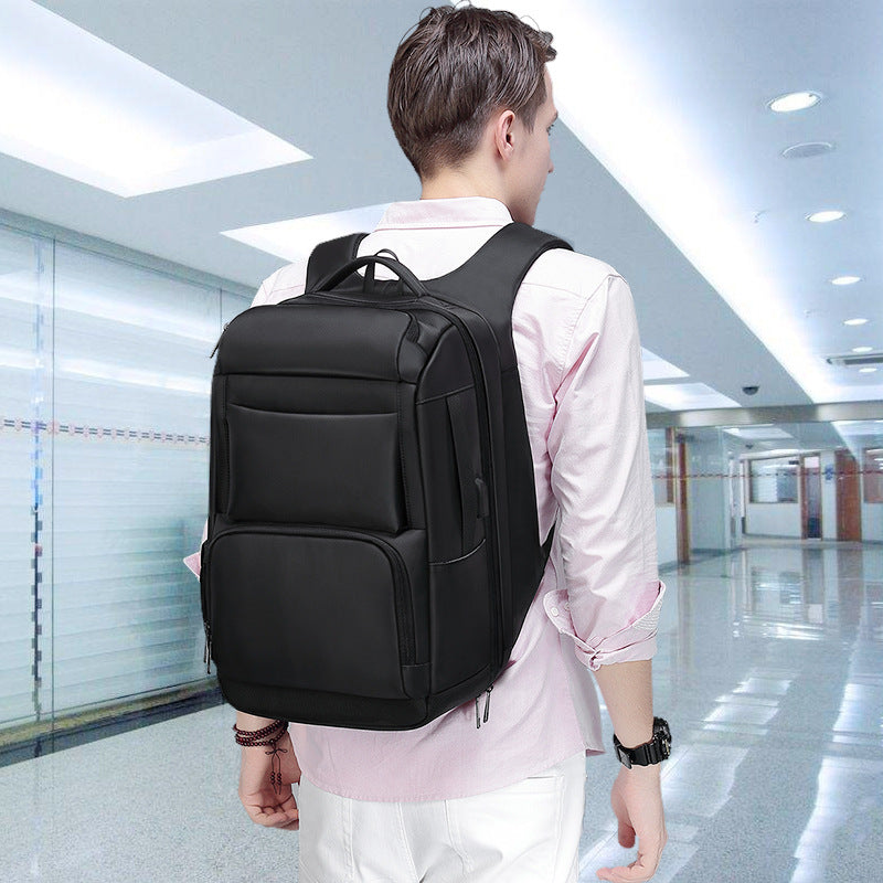 A man wears a sleek, black, minimalist multifunctional backpack with multiple compartments in a bright, modern hallway.
