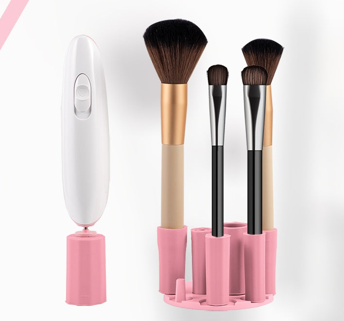 Digitaldistribution375 white electric makeup brush cleaner next to a pink silicone stand holding various brushes.