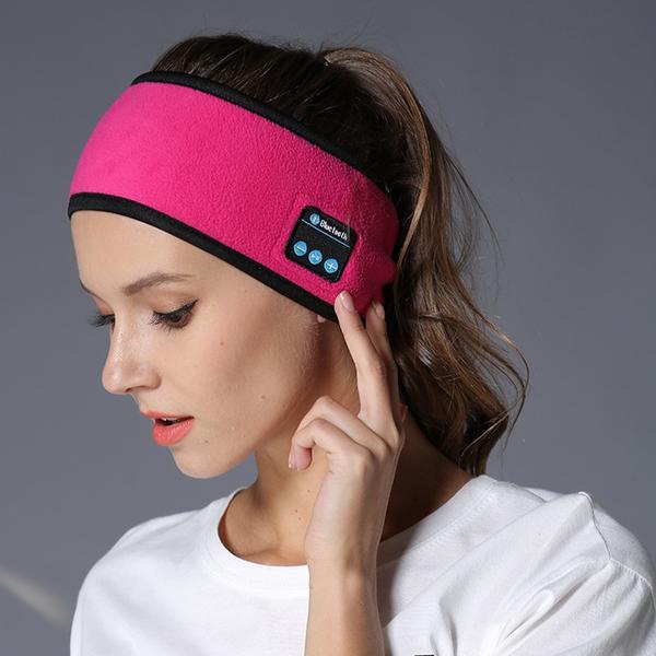 A woman wears a bright pink fleece Bluetooth headband with control buttons, used for fitness or yoga.