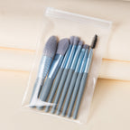 Eight mini makeup brushes with blue handles and grey bristles in a clear, zippered travel pouch.