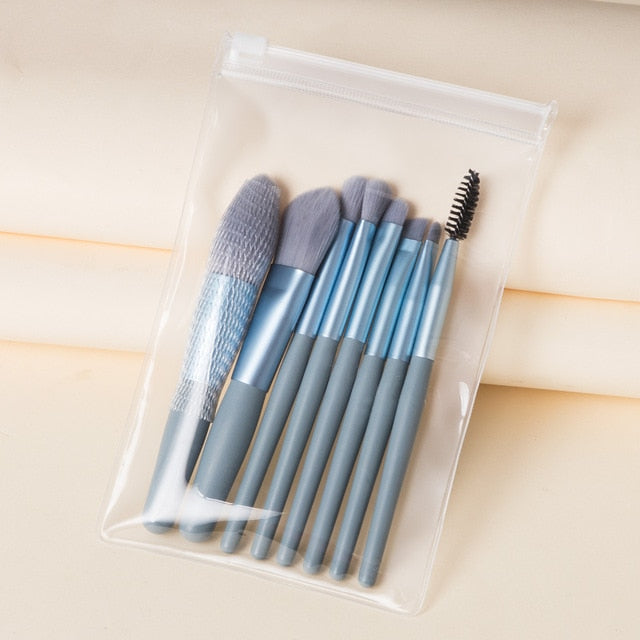 Eight mini makeup brushes with blue handles and grey bristles in a clear, zippered travel pouch.