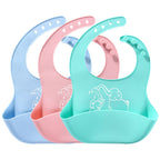 Three pastel silicone baby bibs with elephant prints, featuring adjustable neck straps and deep food-catching pockets.