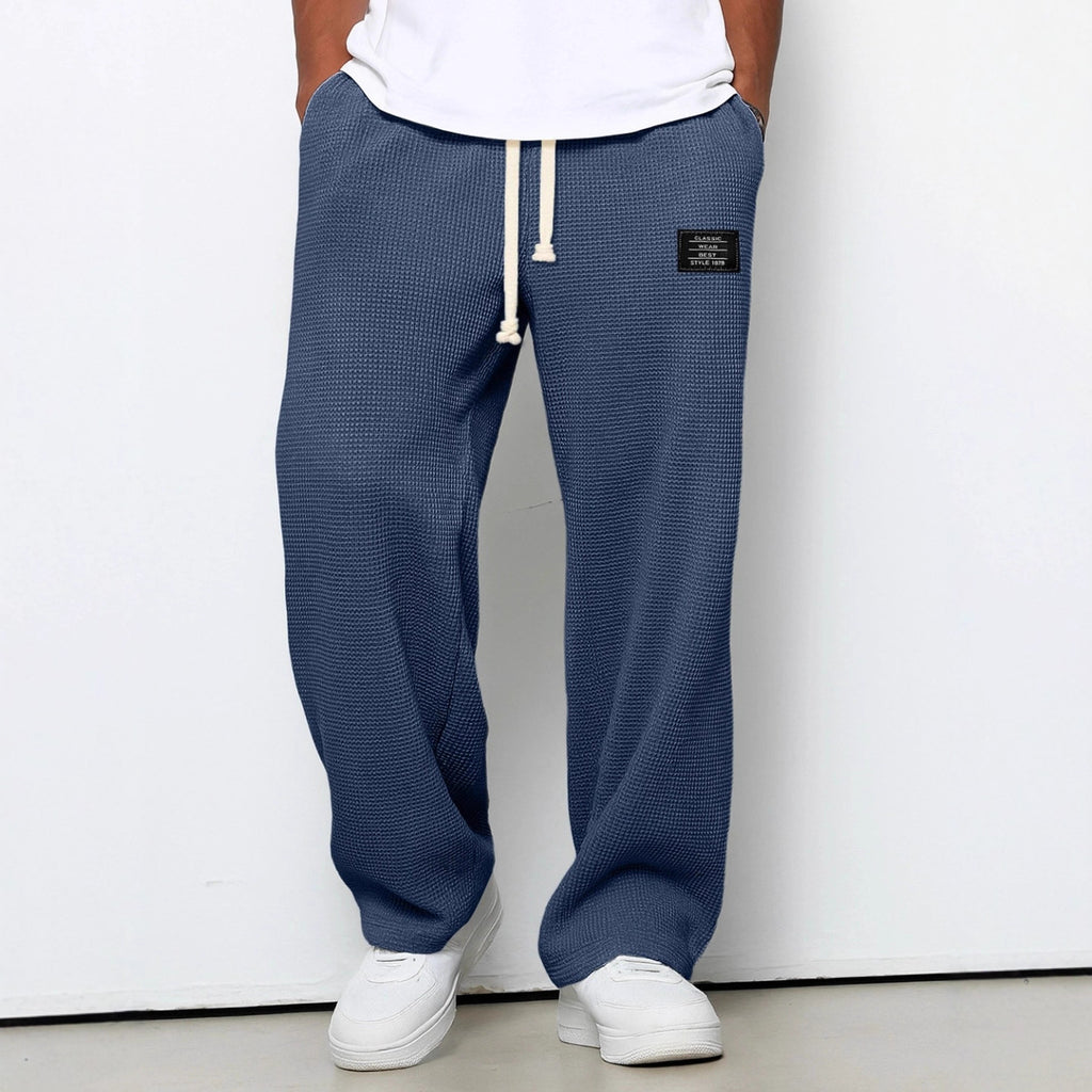 Loose blue waffle-knit trousers with a drawstring waist, side pockets, and a rectangular black brand patch.