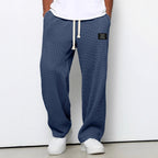 Loose blue waffle-knit trousers with a drawstring waist, side pockets, and a rectangular black brand patch.