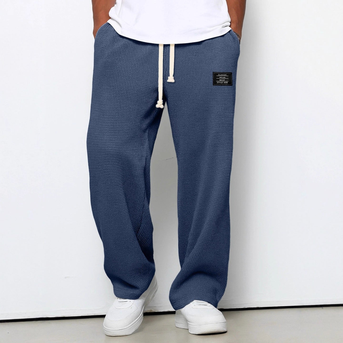 Loose blue waffle-knit trousers with a drawstring waist, side pockets, and a rectangular black brand patch.