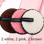 Three round, textured microfiber makeup remover puffs in brown, pink, and white with black "CLEAN SPONGE" finger straps.