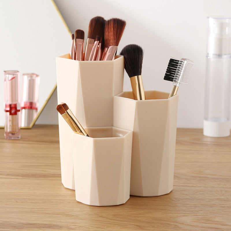 Beige, three-tiered plastic makeup brush organizer with a geometric, faceted design on a wooden desk.