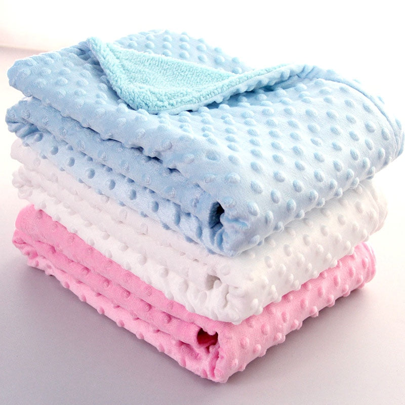 A stack of soft, plush baby blankets in blue, white, and pink with a raised textured dot pattern.
