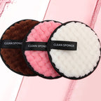 Three round, textured microfiber makeup remover puffs in brown, pink, and white with a black "CLEAN SPONGE" finger band.
