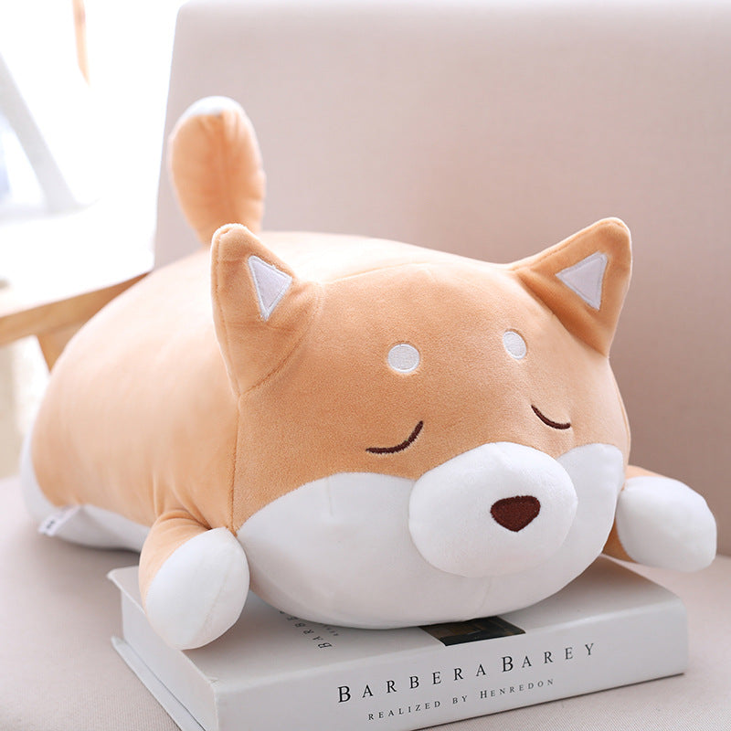 Cute, soft, tan and white Shiba Inu plush pillow lying on a book, featuring closed eyes and a small brown nose.