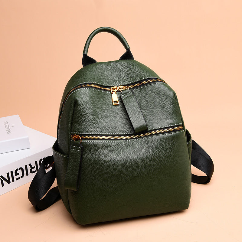 Small dark green pebble leather backpack with gold zippers, a top handle, and black straps on a pale peach background.
