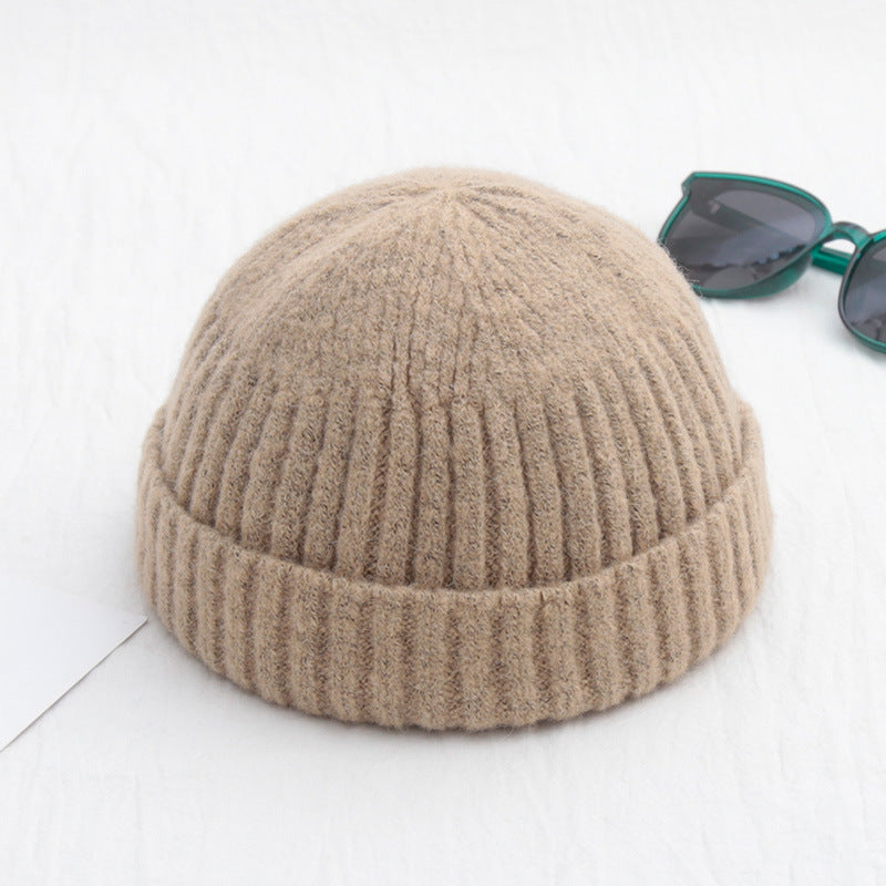 Beige, ribbed-knit, brimless beanie cap next to dark sunglasses on a white background.