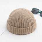 Beige, ribbed-knit, brimless beanie cap next to dark sunglasses on a white background.