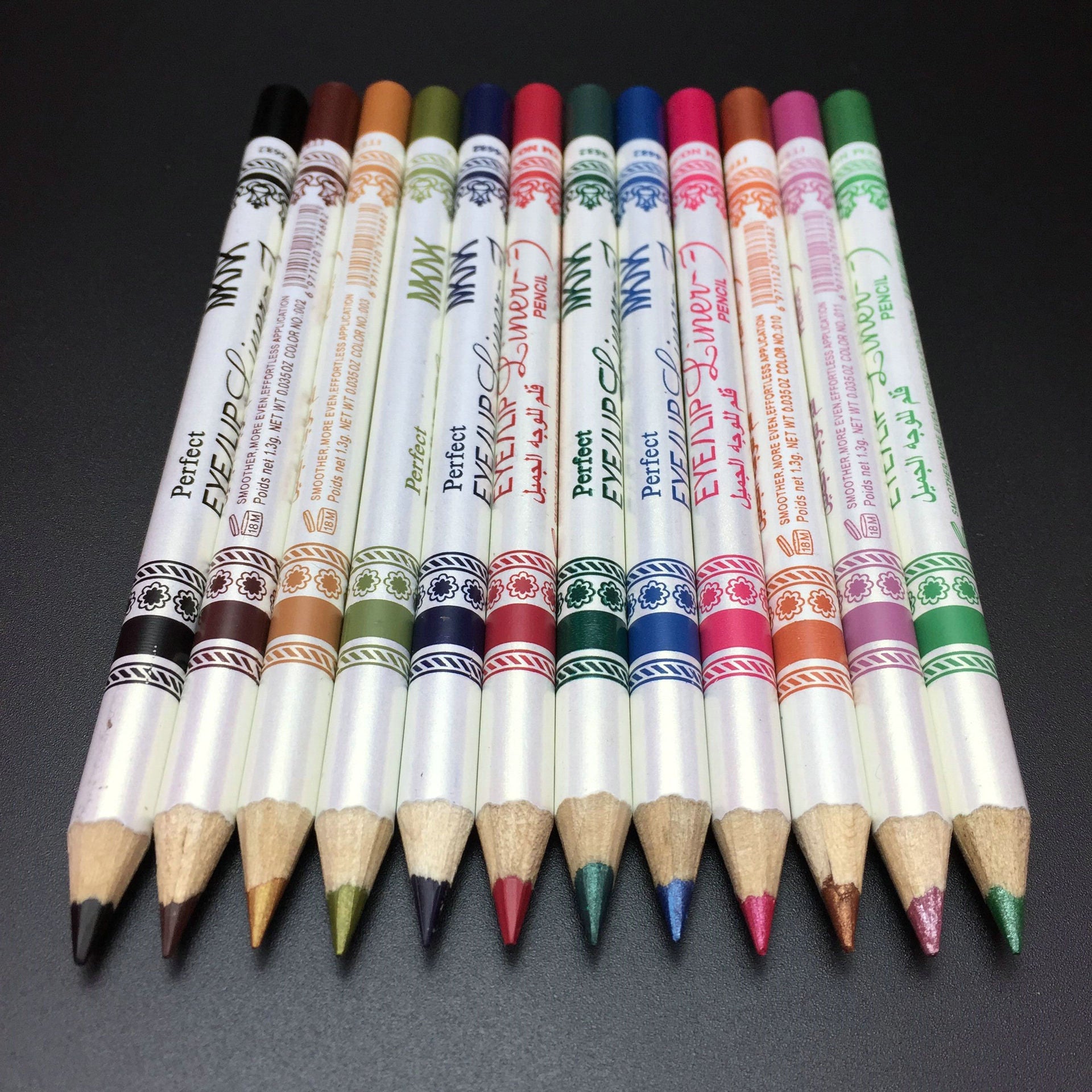 Twelve multi-colored glitter eye and lip liner pencils arranged side-by-side on a black background.