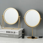 Two round, gold-framed vanity mirrors on a marble surface against a grey background.