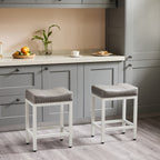 Two grey upholstered saddle bar stools with white steel frames and nailhead trim in a modern grey kitchen.