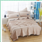 Beige cooling summer quilt with ribbed texture and black trim, styled on a bed with matching pillows in a bright room.