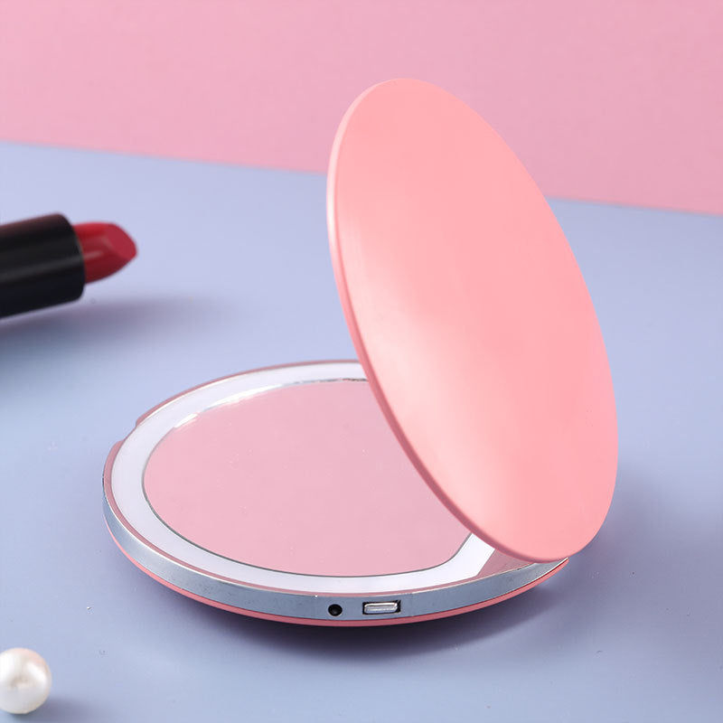 Pink round portable LED makeup mirror with a charging port, set on a blue and pink background.