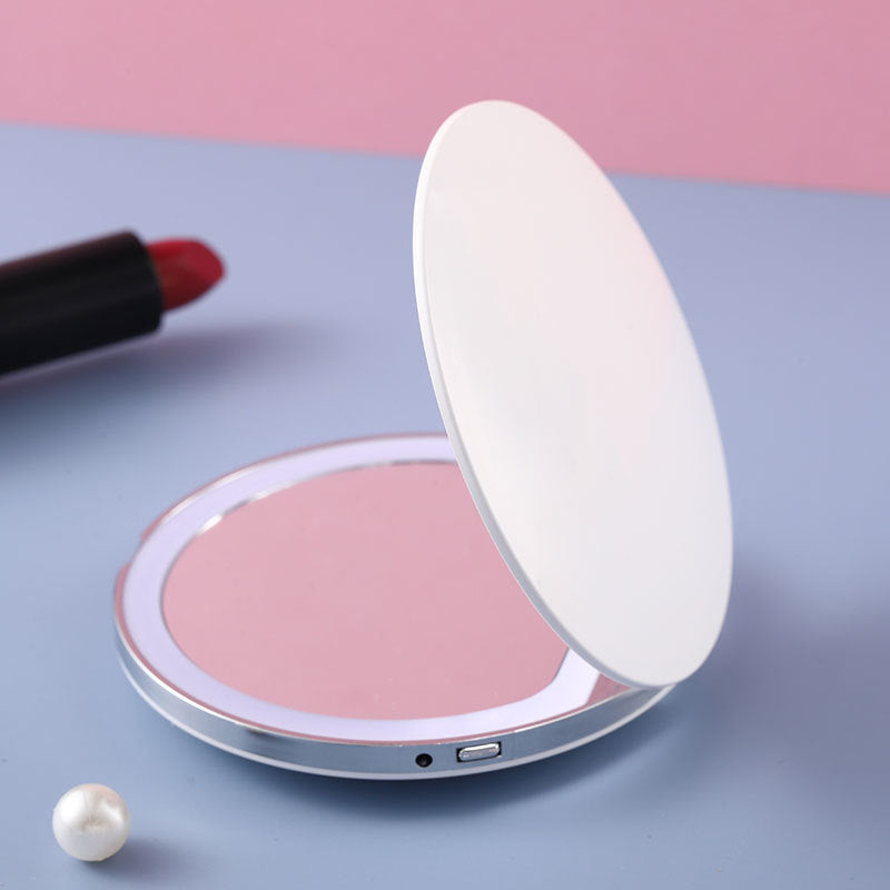 Portable, round white LED makeup mirror with a silver rim, resting on a pastel surface with a lipstick nearby.