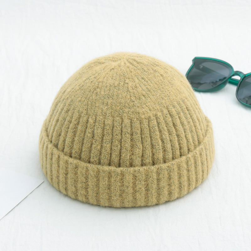Beige ribbed knit beanie hat, styled as a hip-hop docker cap, sitting on a white surface with sunglasses nearby.