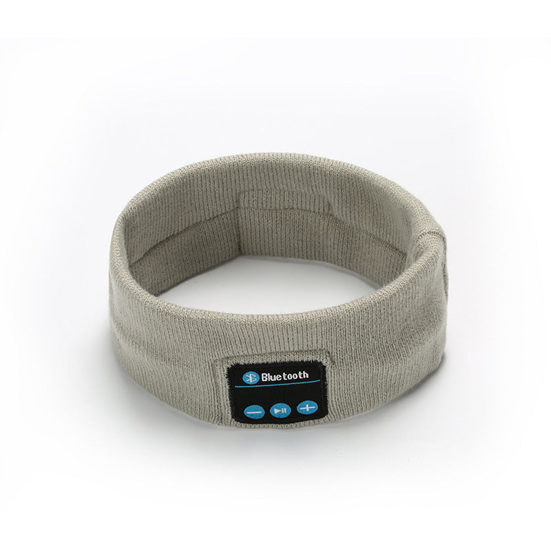 Light grey fabric Bluetooth fitness headband with a front control panel featuring volume and playback buttons.