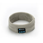 Light grey fabric Bluetooth fitness headband with a front control panel featuring volume and playback buttons.
